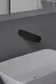 Schwarz beschichtete Wand-Waschtischarmatur von Ideal Standard mit Sensorfunktion, montiert über einem weißen Waschbecken auf grauer Oberfläche.